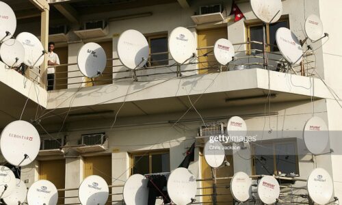 DUBAI, UNITED ARAB EMIRATES - DECEMBER 03:  An expatriot construction worker peers out around satellite dishes used to pick up television channels from India to entertain the workers at a labour camp in Al-Quoz on December 3, 2007 in Dubai, United Arab Emirates. Pakistani and Indian labourers form the backbone of a workforce that over the last few years has transformed Dubai in to a futuristic city that now boasts the tallest building in the world (the Burj Dubai). However, life is hard and many of the workers live in poor conditions in labour camps in areas such as Sharjar and Al-Quoz. This exponential growth in the construction industry has led to problems such as excess traffic and congestion. A metro line is due to be completed in 2008 in an attempt to alleviate the problem.  (Photo by Chris Jackson/Getty Images)