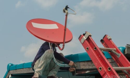 worker-fitting-tv-satellite-dish-to-house-roof-700-136614727