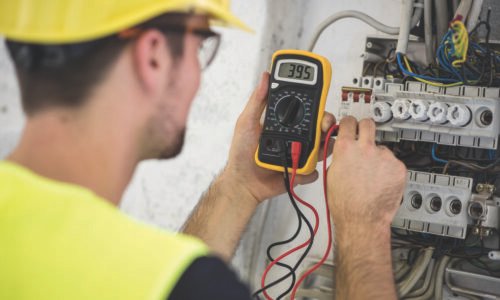 Electrician, wearing protective helmet, glasses and reflective vest testing voltage  on construction site.