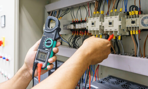 Electrical Engineer adjusts electrical equipment with a multimeter tester in his hand closeup. Professional electrician in electric automation cabinet
