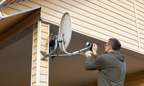 Repairer is repairing satellite TV dish in countryside at summer day.