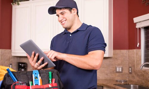 Hispanic repairman or blue collar/service industry worker makes service/house call inside customer's home kitchen. He has his tool box filled with work tools on counter as he uses his digital tablet.  Inspector, exterminator, electrician, plumber, repairmen.  He wears a navy blue uniform.